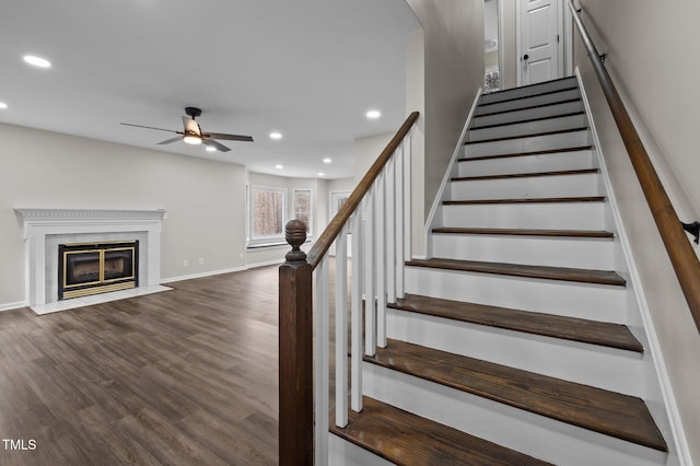 staircase with hardwood / wood-style flooring, ceiling fan, and a fireplace