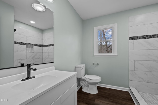 bathroom featuring hardwood / wood-style flooring, tiled shower, vanity, and toilet