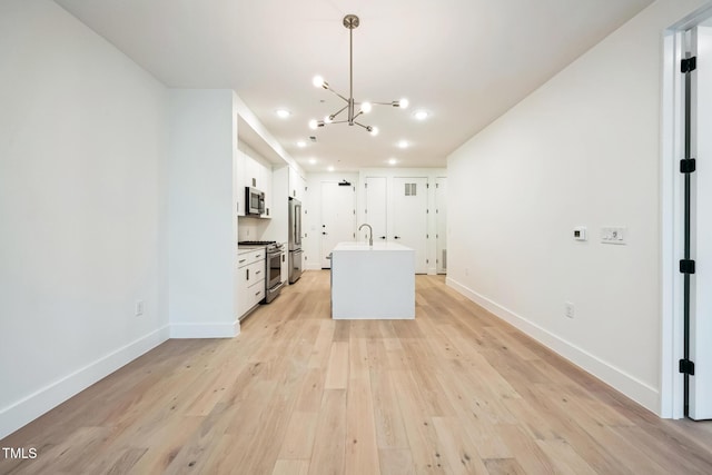 kitchen featuring baseboards, a kitchen island with sink, white cabinets, light wood-style floors, and appliances with stainless steel finishes