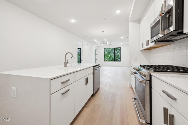 kitchen with light wood-type flooring, a sink, tasteful backsplash, appliances with stainless steel finishes, and light countertops