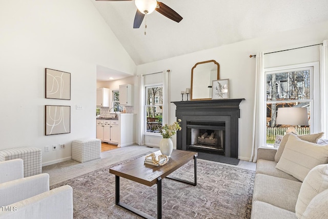 living area featuring a ceiling fan, baseboards, high vaulted ceiling, a fireplace with flush hearth, and light colored carpet