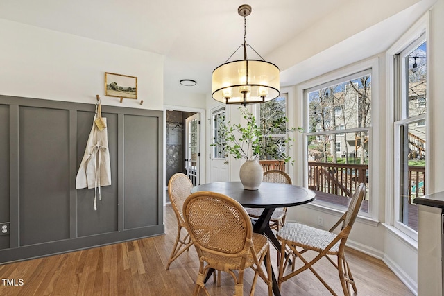 dining room featuring a decorative wall, wainscoting, light wood-type flooring, and a chandelier