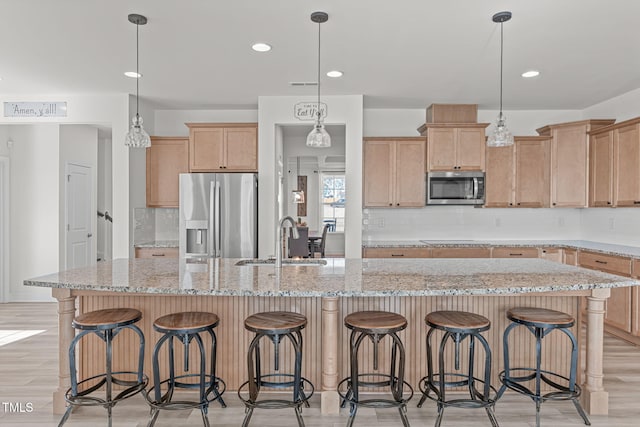 kitchen with sink, decorative light fixtures, stainless steel appliances, and an island with sink