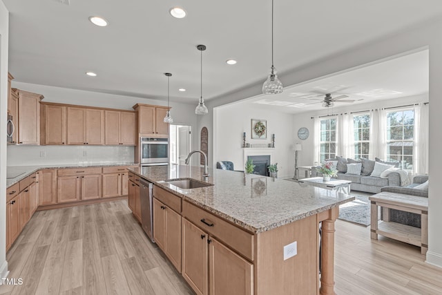 kitchen featuring decorative light fixtures, sink, light stone counters, stainless steel appliances, and a center island with sink