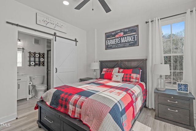 bedroom with ceiling fan, a barn door, light hardwood / wood-style floors, and ensuite bath