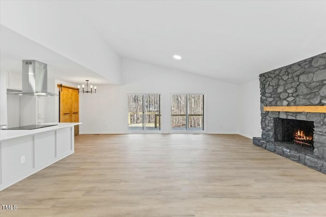 unfurnished living room featuring vaulted ceiling, an inviting chandelier, a fireplace, and light hardwood / wood-style flooring