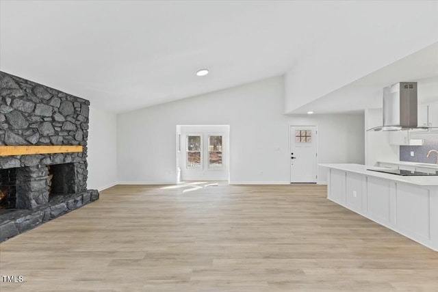 unfurnished living room with lofted ceiling, a stone fireplace, and light hardwood / wood-style floors