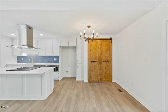 kitchen with sink, island range hood, hanging light fixtures, black electric cooktop, and white cabinets