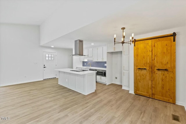 kitchen with light hardwood / wood-style flooring, white cabinetry, island range hood, a kitchen island, and decorative light fixtures