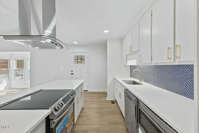 kitchen with appliances with stainless steel finishes, island range hood, white cabinetry, sink, and light hardwood / wood-style floors