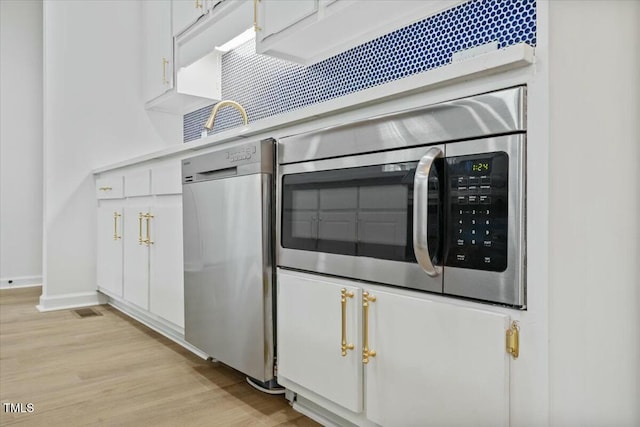 kitchen with stainless steel appliances, white cabinetry, and light hardwood / wood-style floors