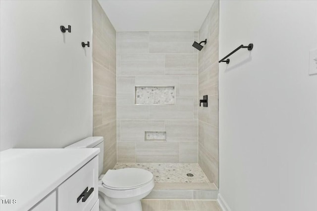 bathroom with a tile shower, vanity, and toilet