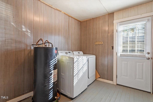 clothes washing area with separate washer and dryer, light wood-type flooring, water heater, and wood walls