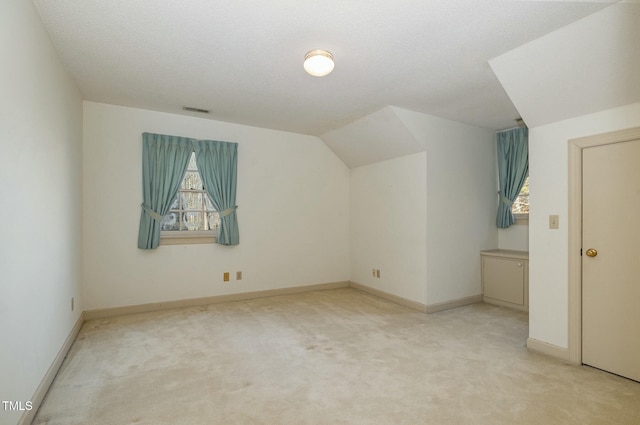 additional living space featuring light colored carpet, vaulted ceiling, and a textured ceiling