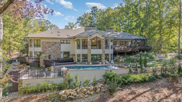 back of property with a deck, a sunroom, an outdoor pool, and stone siding