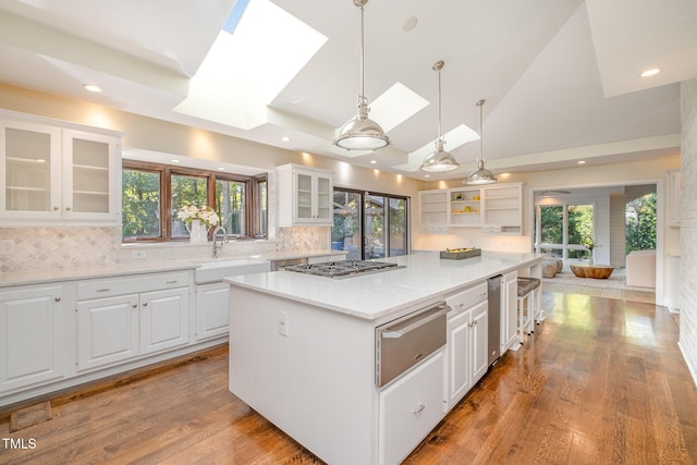 kitchen with decorative light fixtures, a skylight, sink, white cabinets, and a center island