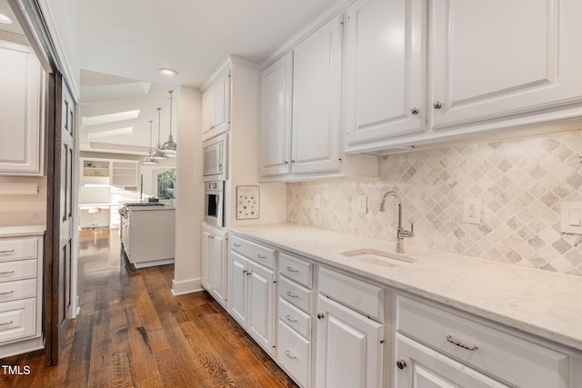 kitchen with sink, white cabinetry, dark hardwood / wood-style flooring, light stone countertops, and decorative backsplash