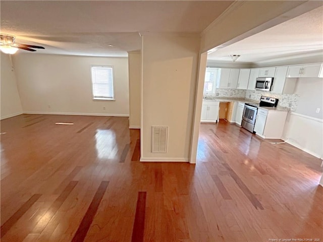 interior space with appliances with stainless steel finishes, white cabinetry, backsplash, ceiling fan, and light hardwood / wood-style flooring