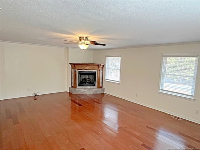 unfurnished living room featuring ceiling fan, wood-type flooring, ornamental molding, and a textured ceiling