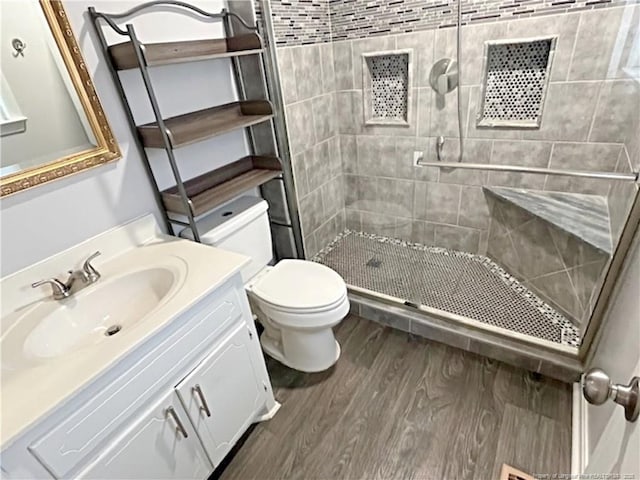 bathroom with vanity, wood-type flooring, toilet, and tiled shower