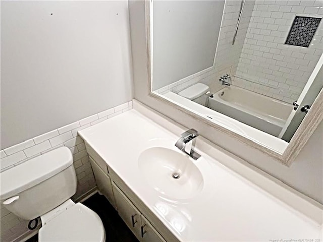 full bathroom with tile walls, vanity, tiled shower / bath combo, and toilet