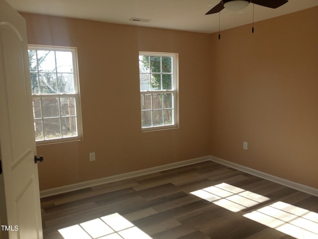 unfurnished room with wood finished floors, visible vents, a wealth of natural light, and baseboards