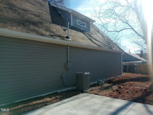 view of side of property featuring cooling unit, fence, a patio area, and a shingled roof