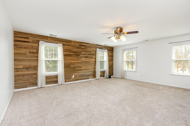 carpeted spare room with visible vents, wood walls, a ceiling fan, and baseboards