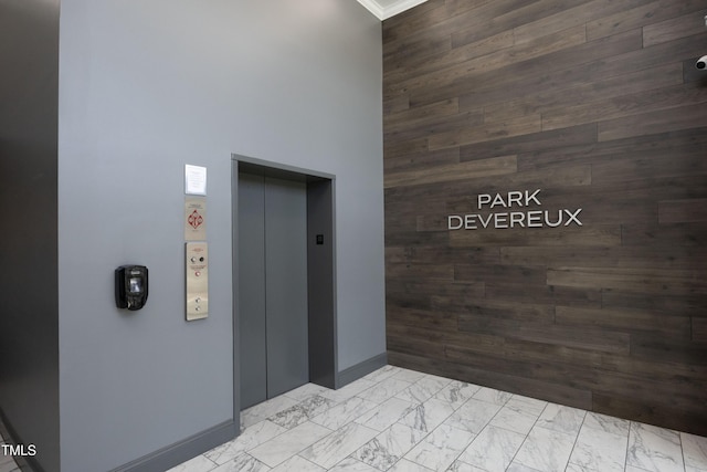 hallway with marble finish floor, a high ceiling, elevator, and wood walls