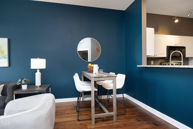 dining space featuring track lighting, dark wood-style flooring, and baseboards