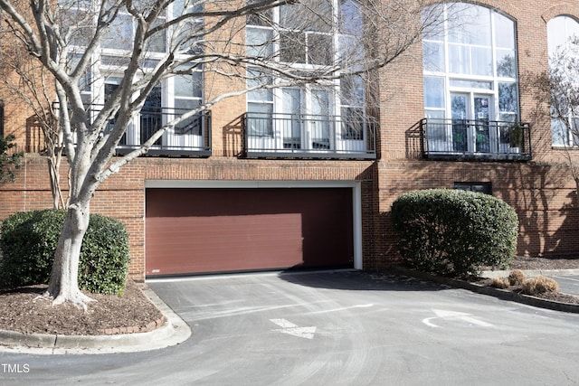 multi unit property with a garage, driveway, brick siding, and a balcony