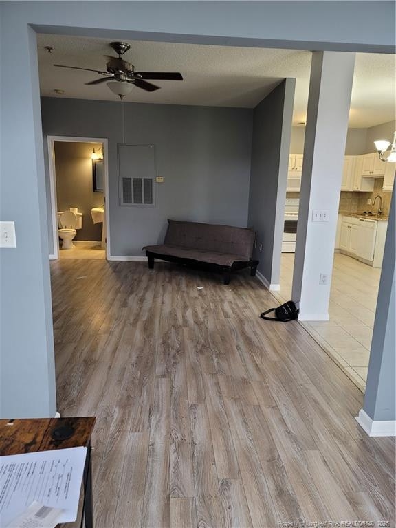 unfurnished living room featuring sink, ceiling fan with notable chandelier, and light wood-type flooring