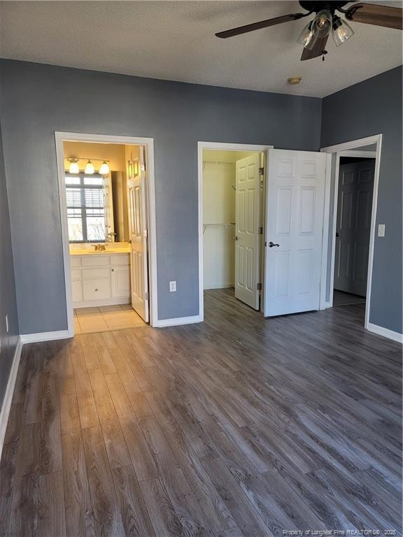 unfurnished bedroom featuring hardwood / wood-style flooring, ceiling fan, connected bathroom, a spacious closet, and a closet