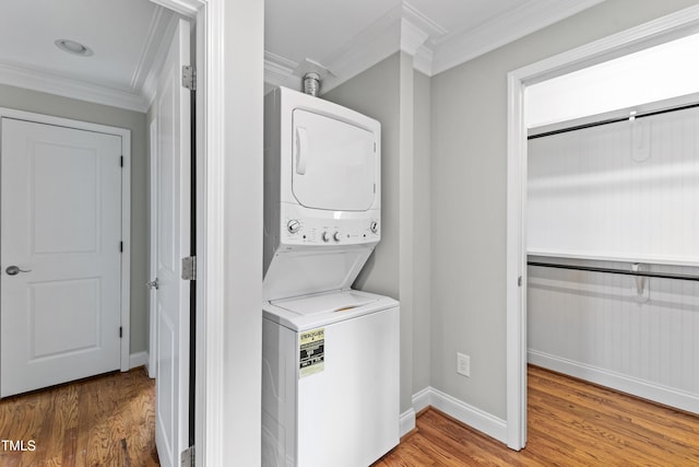 laundry area featuring ornamental molding, light hardwood / wood-style floors, and stacked washing maching and dryer