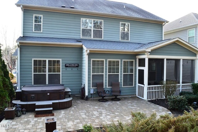 rear view of house featuring roof with shingles, a patio area, a sunroom, and a hot tub