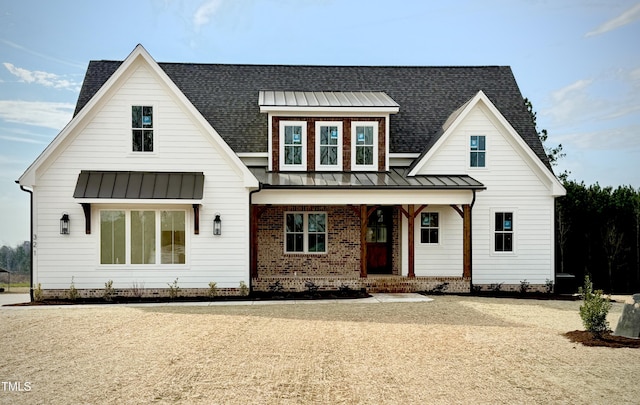 modern farmhouse style home featuring a shingled roof, a standing seam roof, brick siding, and metal roof