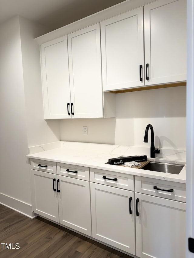 kitchen featuring light stone counters, dark wood-style flooring, a sink, and white cabinets