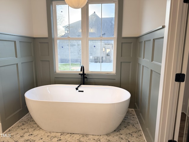 bathroom featuring a freestanding tub, a decorative wall, and a wainscoted wall