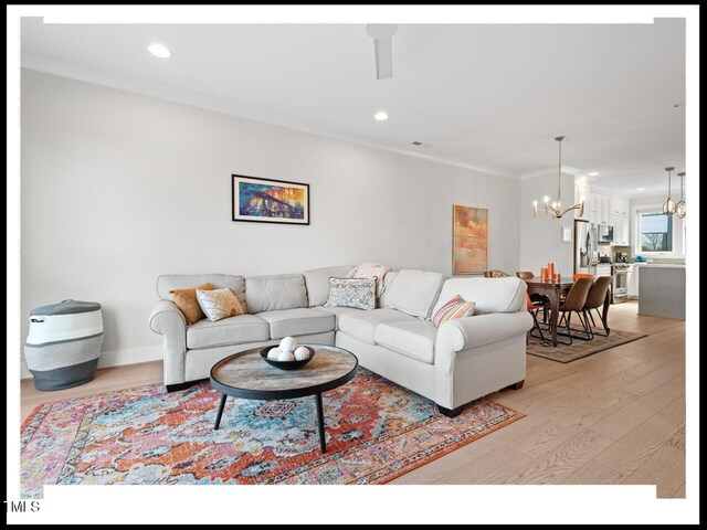 living room with ornamental molding, an inviting chandelier, and light hardwood / wood-style floors