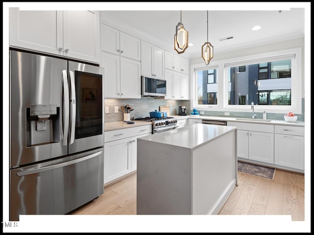 kitchen featuring a kitchen island, appliances with stainless steel finishes, pendant lighting, white cabinetry, and sink