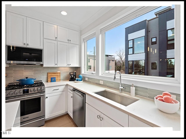 kitchen with sink, white cabinetry, backsplash, stainless steel appliances, and ornamental molding