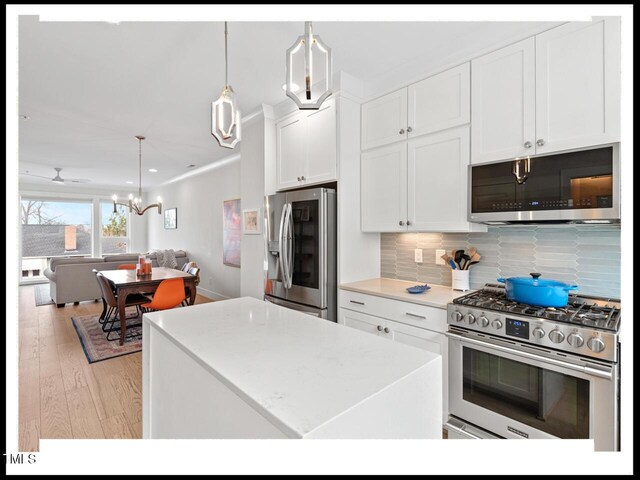 kitchen with white cabinetry, hanging light fixtures, light wood-type flooring, stainless steel appliances, and backsplash