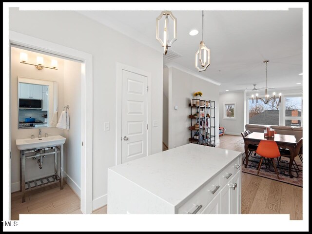 kitchen with white cabinetry, a center island, hanging light fixtures, light hardwood / wood-style flooring, and a notable chandelier