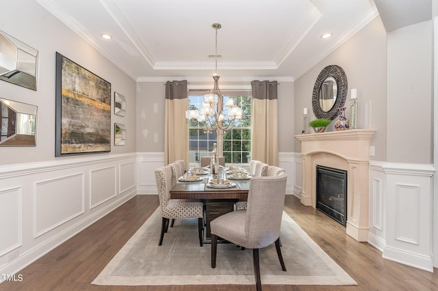 dining space featuring an inviting chandelier, a tray ceiling, ornamental molding, and hardwood / wood-style flooring