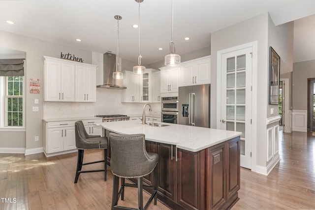 kitchen with white cabinets, stainless steel appliances, sink, and wall chimney range hood