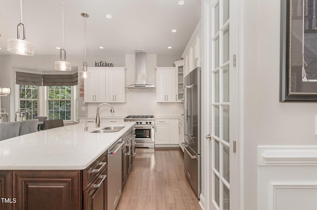 kitchen with wall chimney range hood, sink, white cabinetry, dark brown cabinets, and high quality appliances