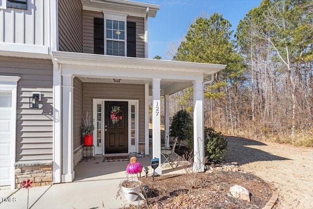 entrance to property with a garage, stone siding, and covered porch