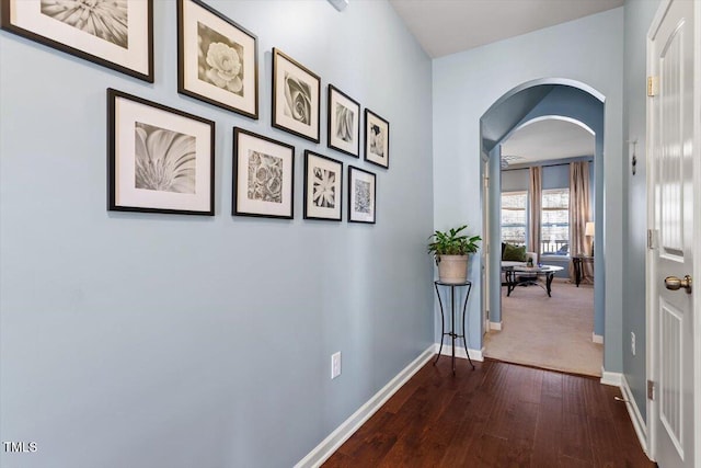 hall featuring arched walkways, dark wood finished floors, and baseboards