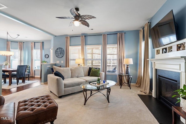 living area featuring light carpet, a fireplace with flush hearth, a ceiling fan, and baseboards