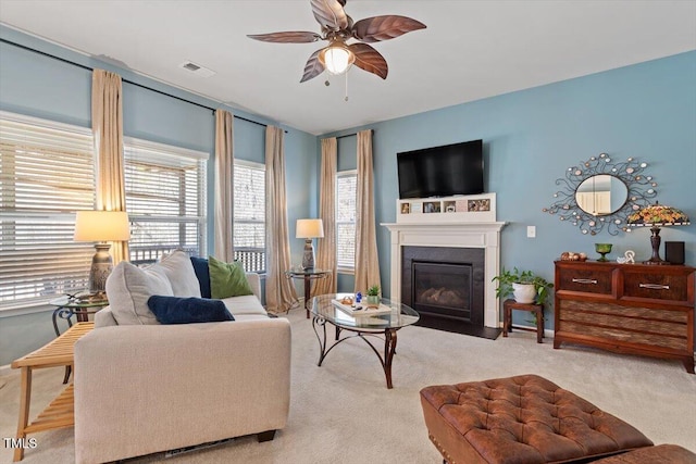 living room featuring ceiling fan, light carpet, a fireplace with flush hearth, and visible vents